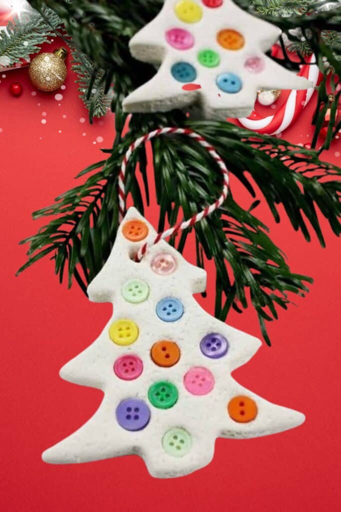 Handmade air dry clay Christmas tree ornament decorated with colorful buttons hanging from pine branches against a red background  a fun DIY craft for kids.