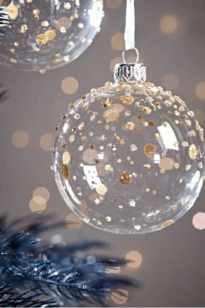 Clear glass Christmas ornament with gold glitter dots hanging on a Christmas tree branch — elegant DIY holiday decoration idea.