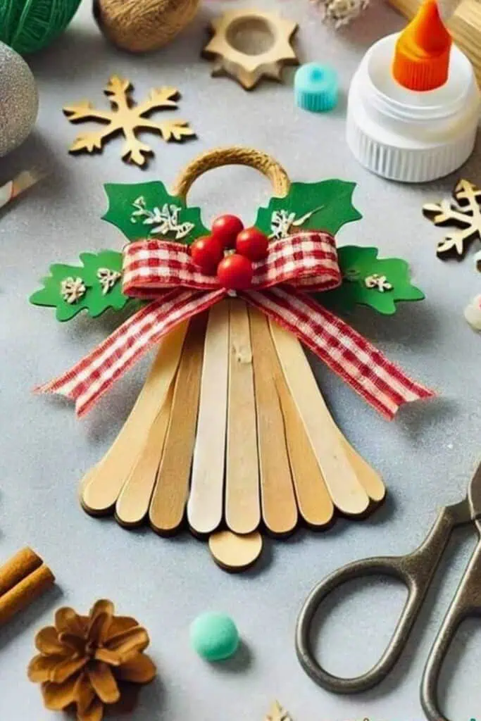 Easy DIY Christmas Ornament made out of popsicle sticks in the shape of a bell decorated with construction paper, ribbon and faux berries.