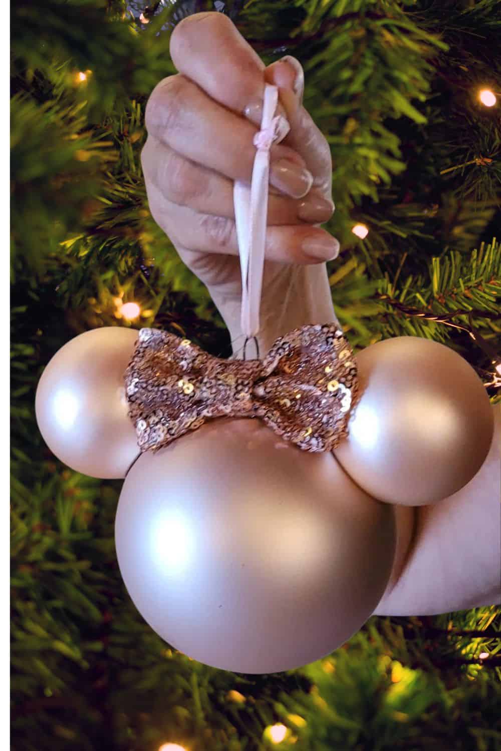 DIY Minnie Mouse Christmas ornament made with shiny gold baubles and a sparkly sequin bow, hanging on a festive Christmas tree. A cozy, elegant Disney-inspired holiday craft idea perfect for Pinterest.