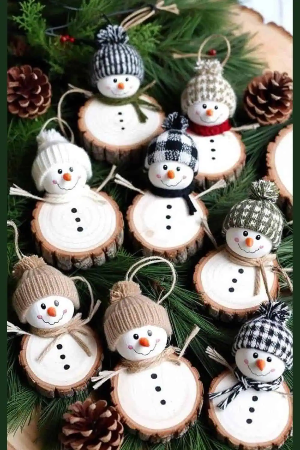 Handmade DIY wood slice snowman Christmas ornaments featuring painted snowman faces with mini winter hats and scarves, arranged on evergreen branches with pinecones — perfect for rustic holiday decor or craft