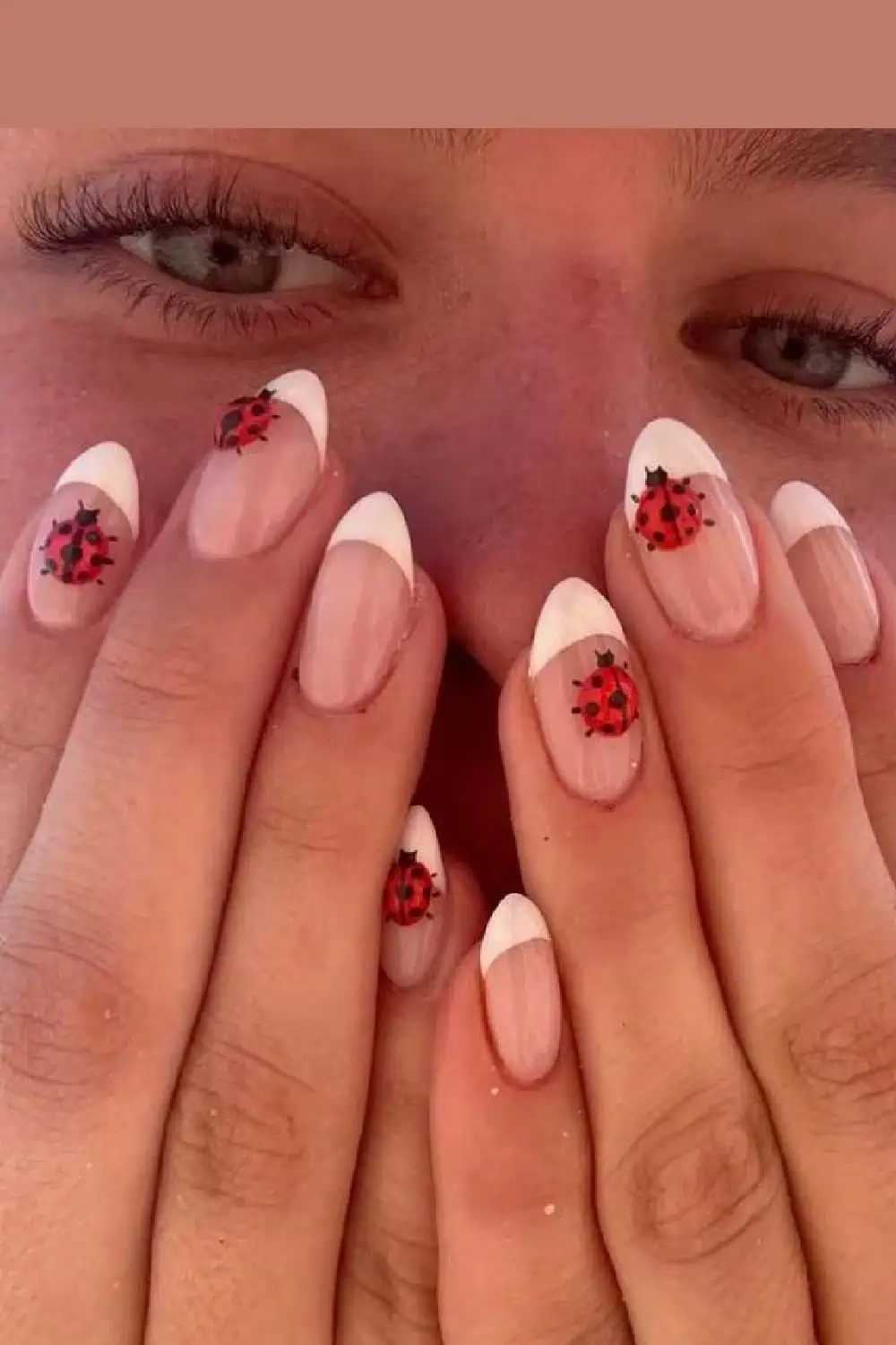 Close-up of almond-shaped nails with a white French tip design, featuring hand-painted red and black ladybug nail art for a playful summer aesthetic.