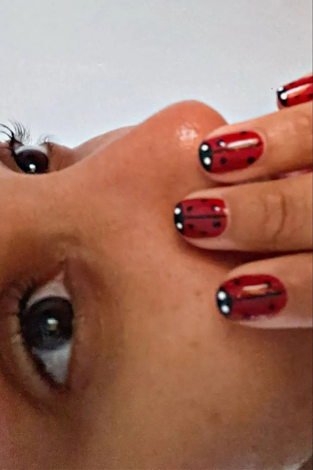 Close-up of a summer ladybug nail design featuring short red nails with black spots, a black center line, and white accent dots at the tips, inspired by the ladybug summer aesthetic.