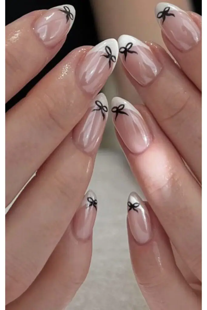 Delicate pink french manicure with a black bow design on each nail