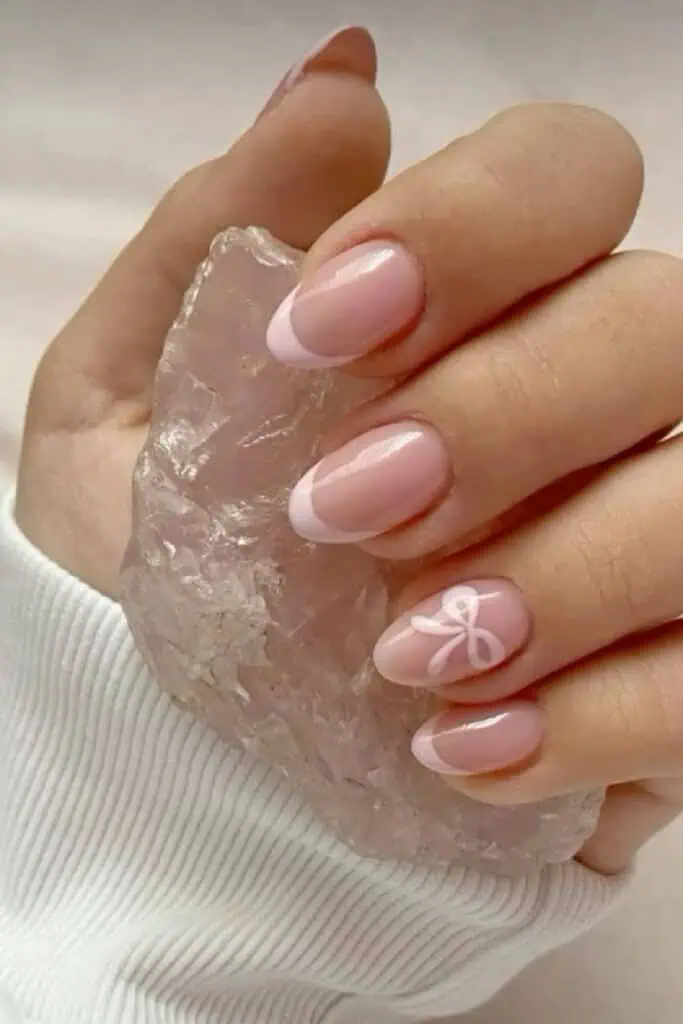 Light pink french manicure with a pink bow design on an accent nail