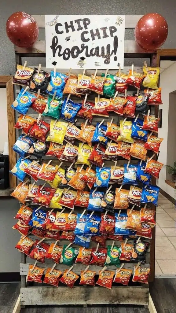 Graduation party chip display using pallet wood with individual chip bags clipped on, decorated with a "Chip Chip Hooray!" sign easy and fun DIY snack station idea.