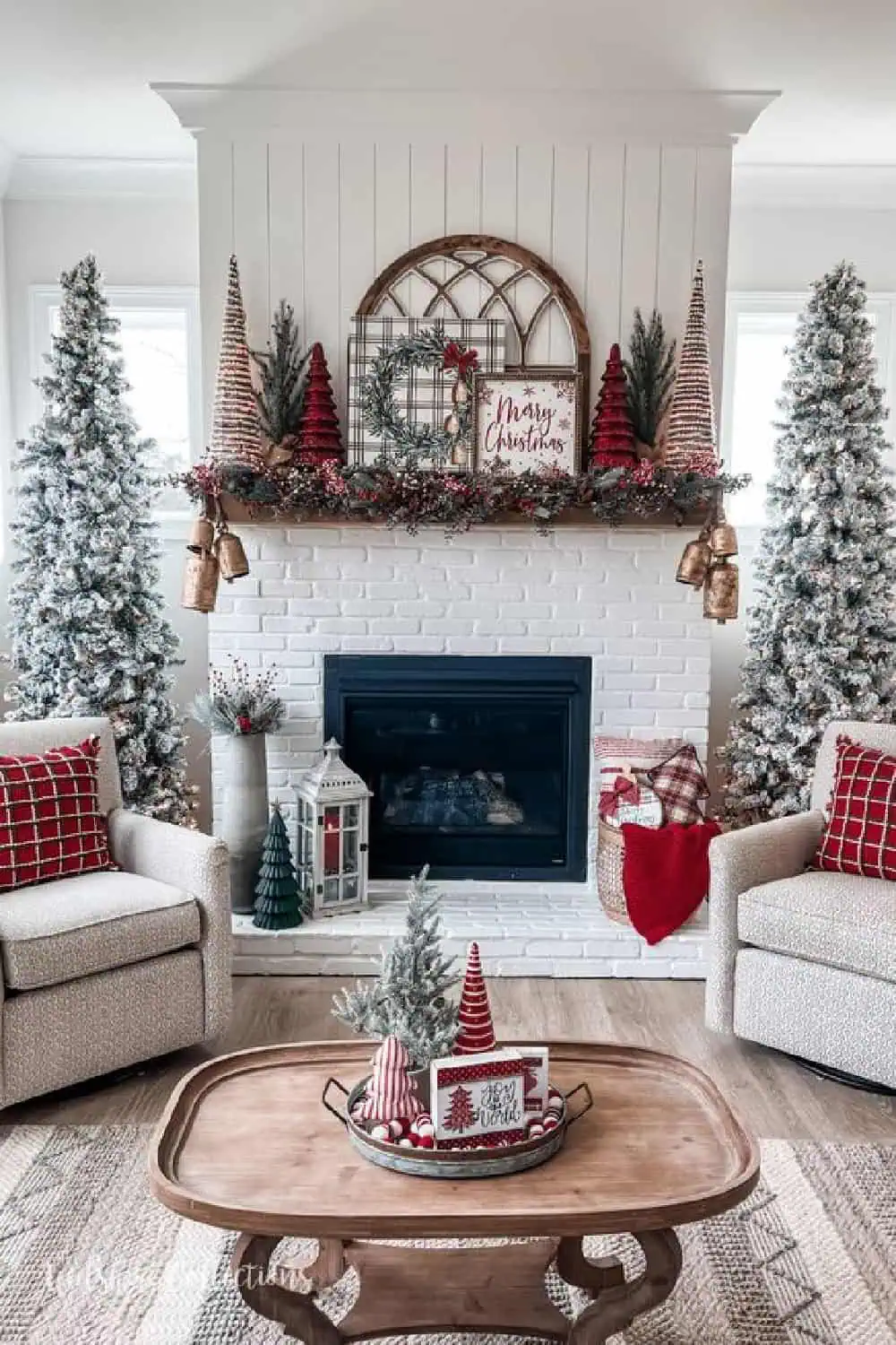 white farmhouse living room with white flocked trees, a decorated mantel and red pillows.