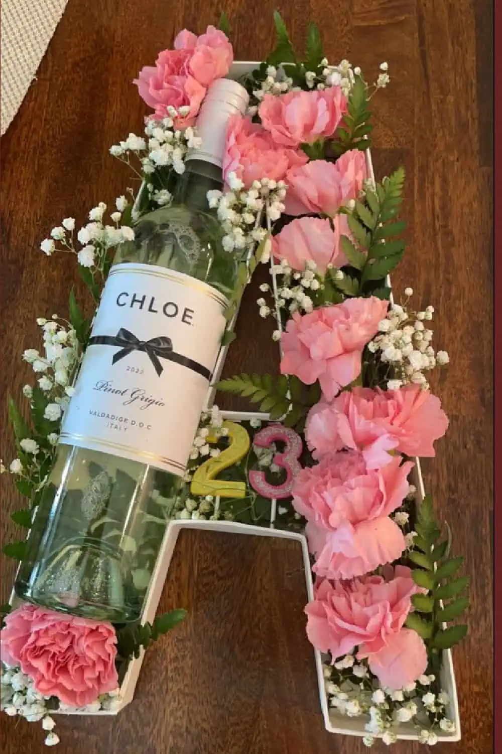 Letter A shaped gift box filled with pink flowers, babys breath and a bottle of wine