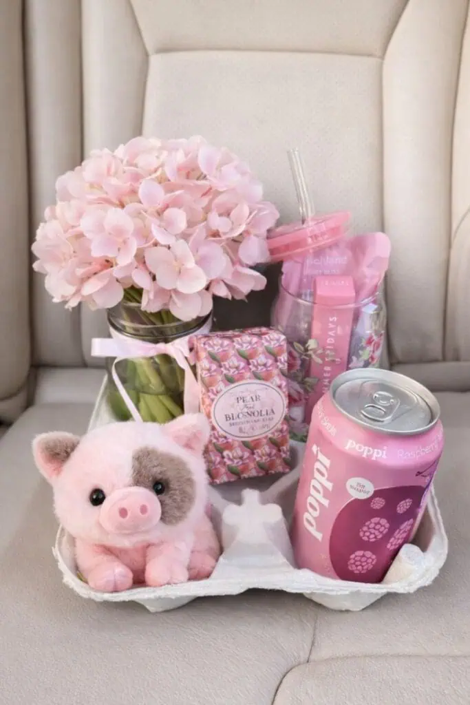 Aesthetic pink gift basket with hydrangea flowers, plush pig, candle, drink, and self care items arranged in a cute cup holder tray