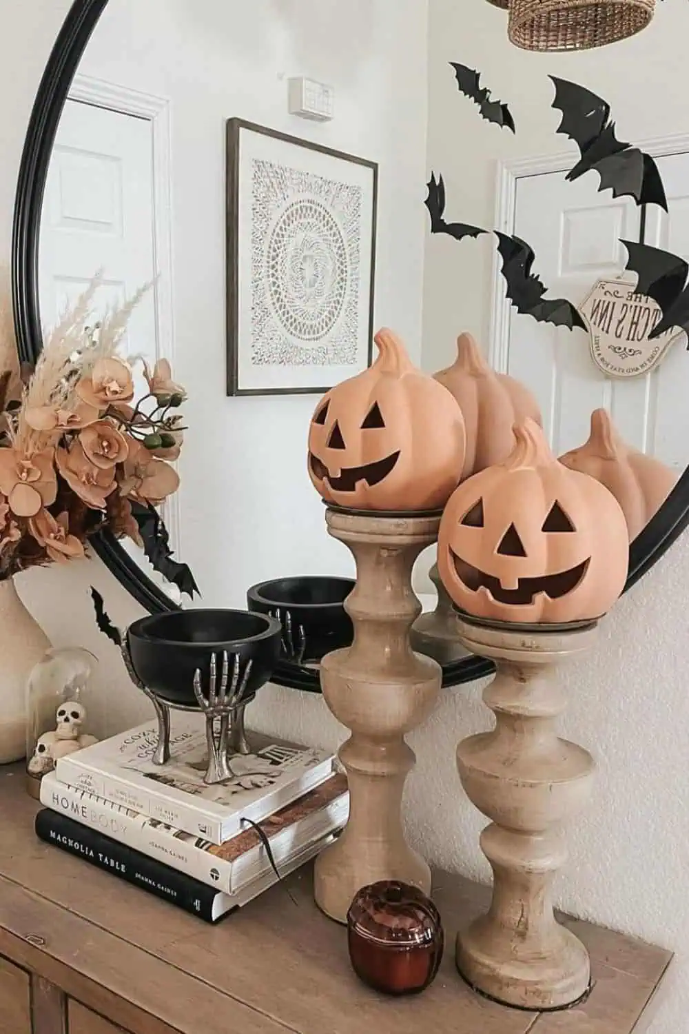 Neutral fall crafts and Halloween decor entryway with jack-o’-lantern pumpkins on wooden stands, dried floral arrangement, skull accents, and bat wall decorations.