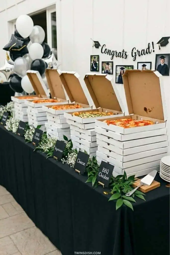 Graduation party pizza buffet with stacked pizza boxes, black tablecloth, and a 'Congrats Grad!' banner