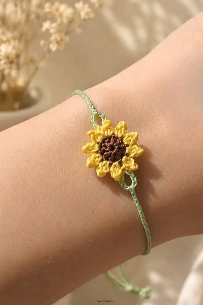 Handmade crochet sunflower bracelet with yellow petals and brown center worn on a wrist with sage green braided cord