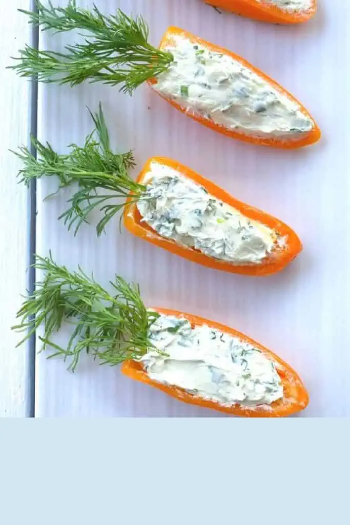 Orange bell peppers sliced in a carrot stick shape filled with cream cheese mix and topped with a branch of dill on the end to look like a carrot