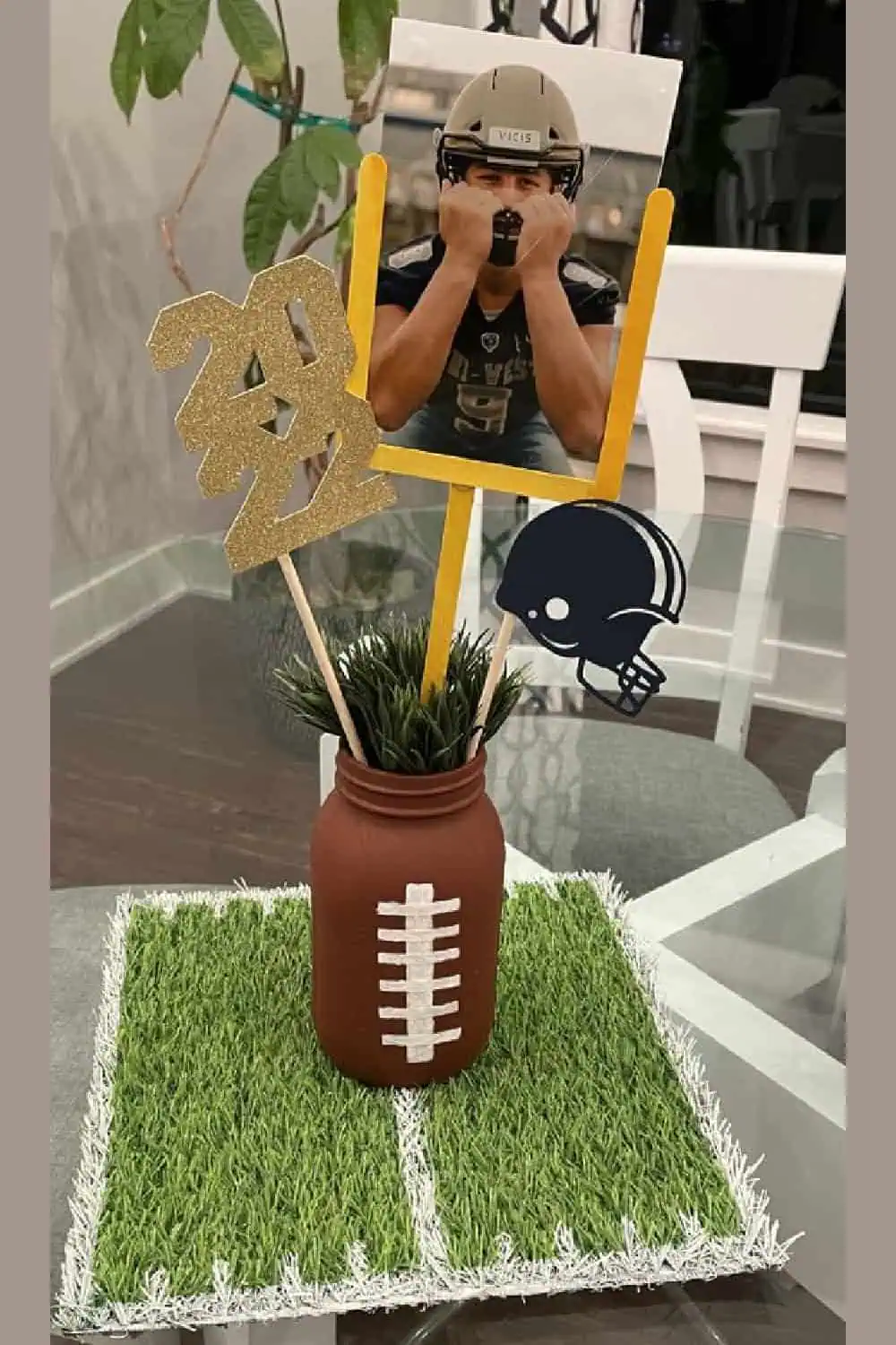 Diy football theme graduation party centerpiece for guys with a mason jar painted to look like  football a picture of the guy and a astroturf mat painted with white markings to look like a football field