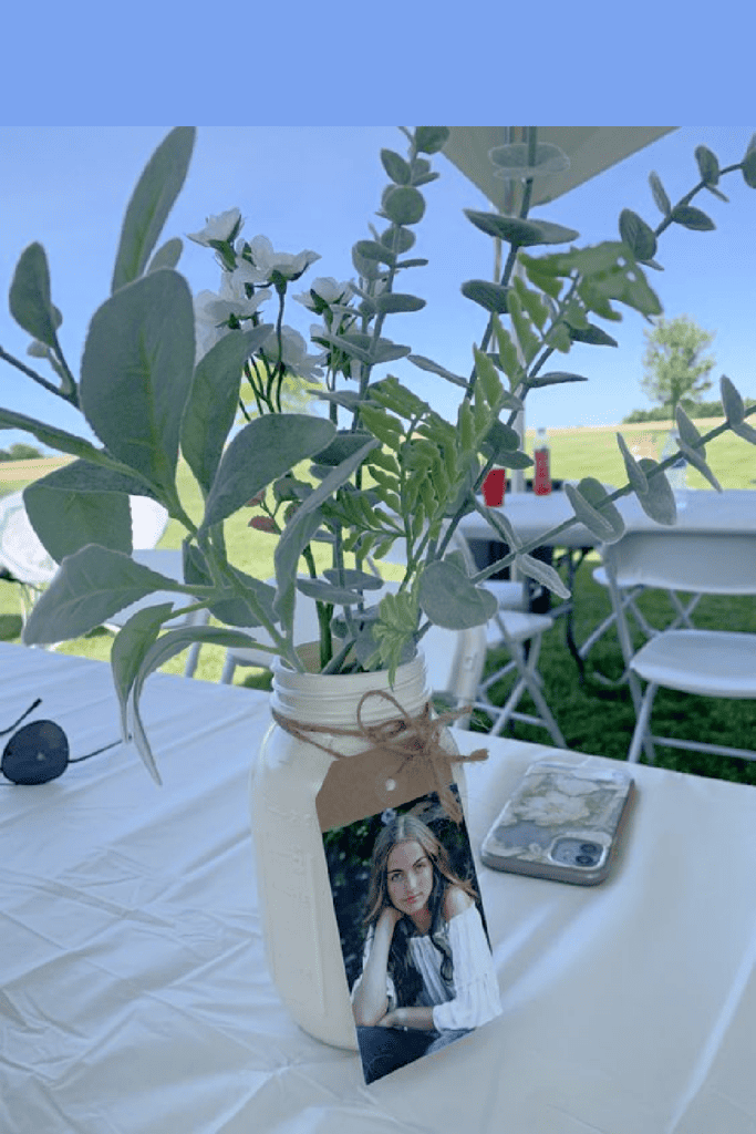 Graduation party jar centerpiece with twine, a picture, and eucalyptus stems and flowers on a table