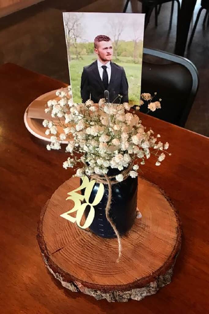 Graduation party centerpiece for guys with a black mason jar, baby's breath, a photo, and a wood slab