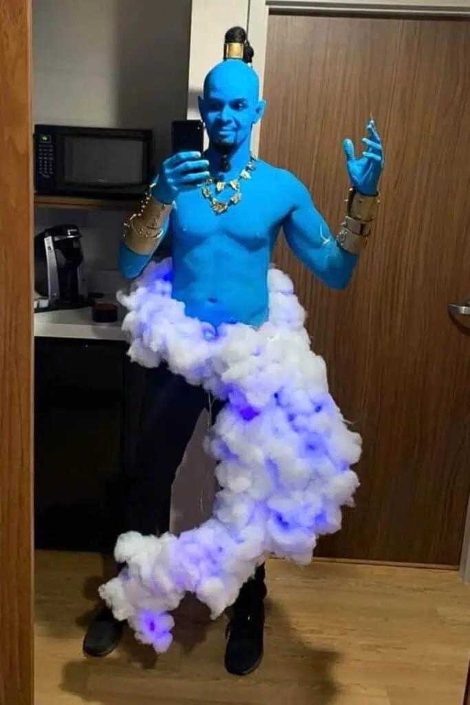 Creative DIY Genie Halloween costume for men featuring bright blue body paint, gold accessories, and a cloud of glowing cotton at the waist to mimic a magical floating effect. Inspired by Aladdin and trending this year male costume ideas.