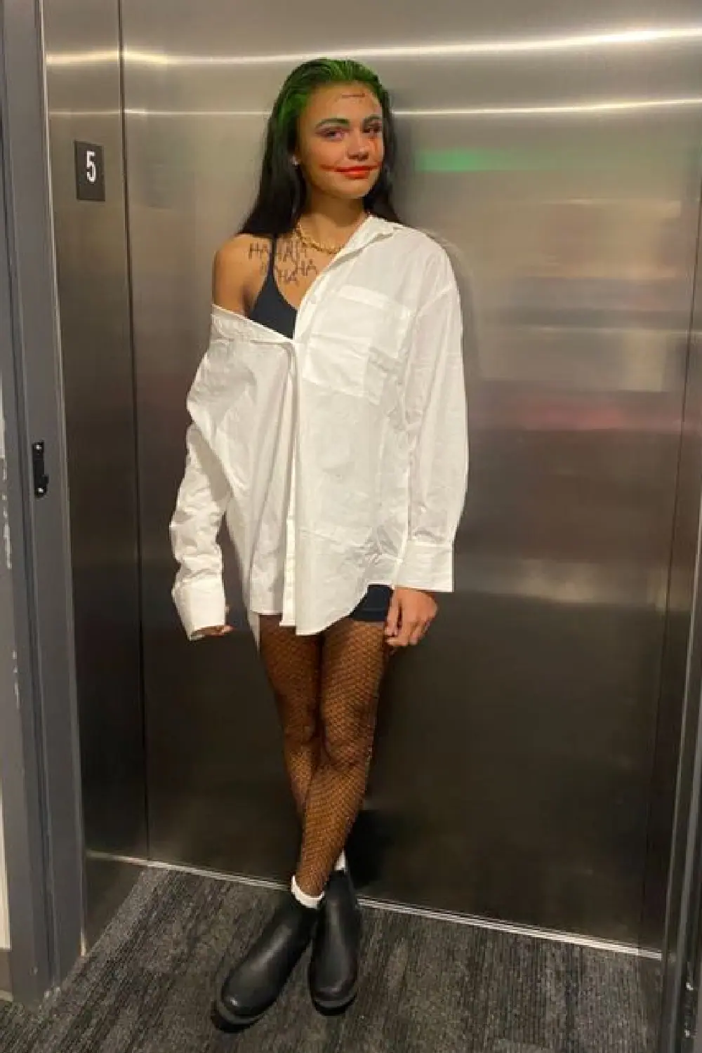Woman in Joker Halloween costume with white shirt, green hair, and boots