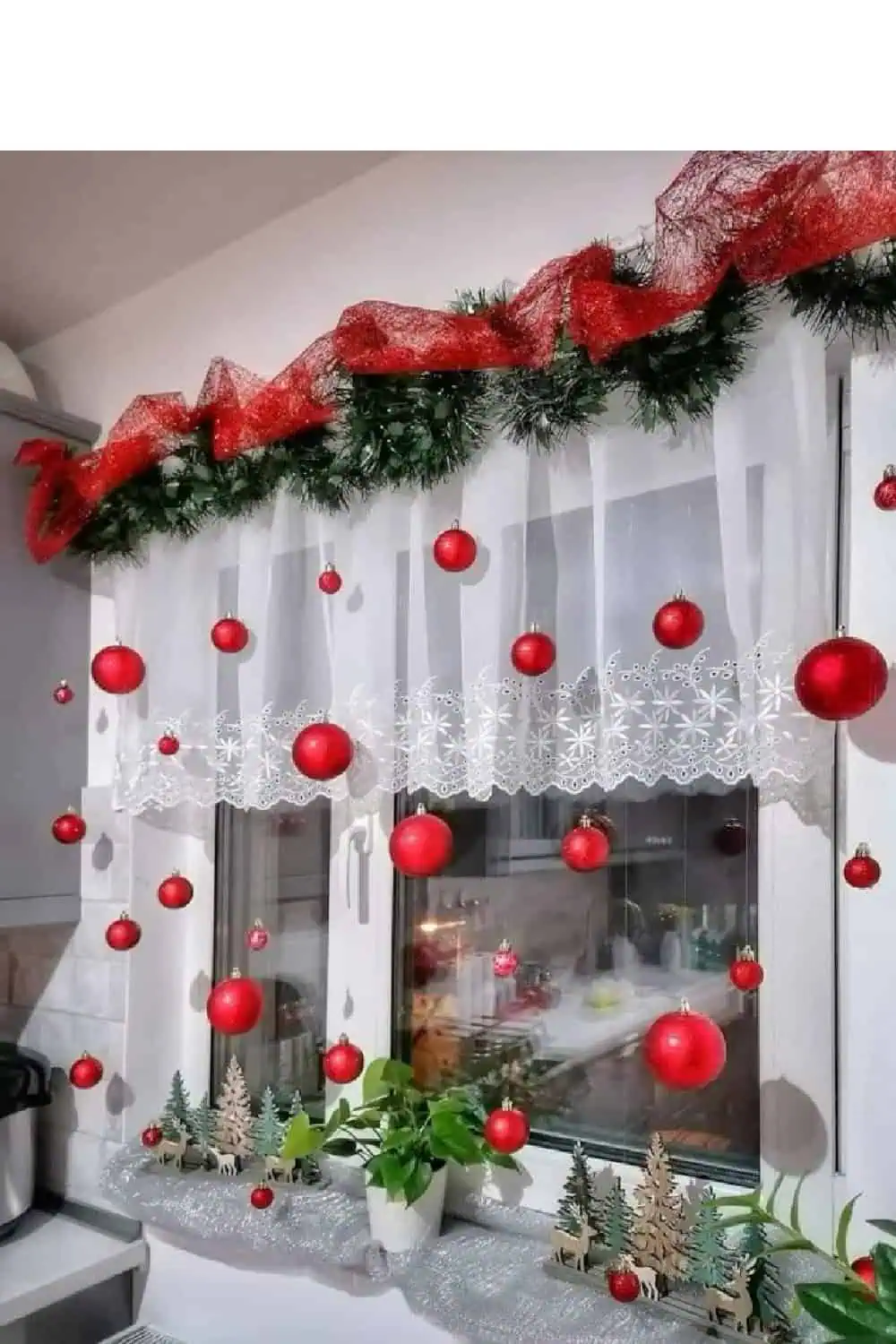 Christmas garland with red ribbon and hanging red ornaments decorating a kitchen window