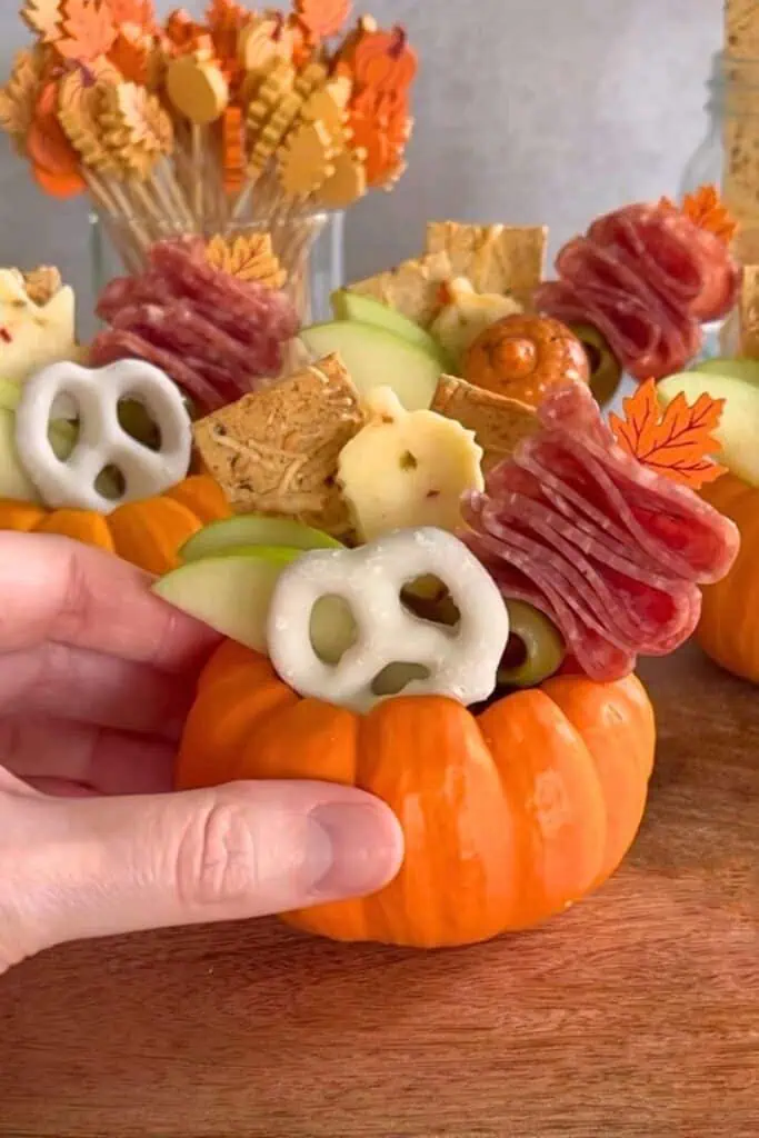 Pumpkin-shaped charcuterie cup filled with salami, cheese, apple slices, pretzels, and crackers, styled as a festive fall and Thanksgiving appetizer.