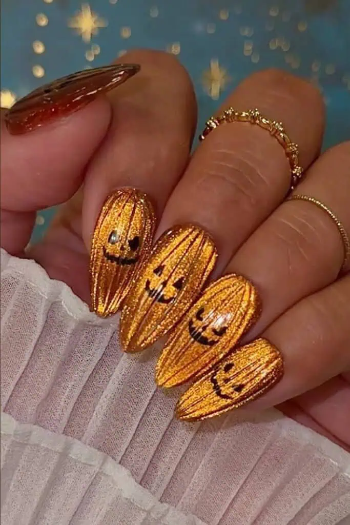 Close-up of a hand with glittery orange Halloween nails featuring black pumpkin faces and a shimmery tiger-eye finish — festive fall nail art design.