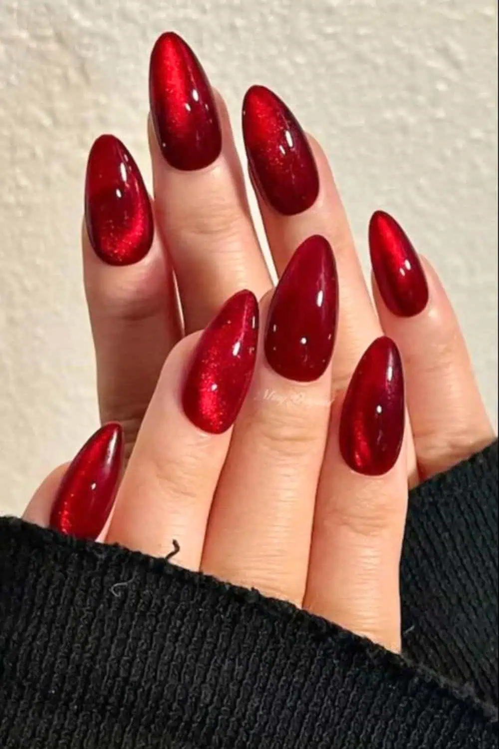 Glossy almond-shaped deep red nails with a rich burgundy finish, styled with a cozy black sweater sleeve. A chic and timeless fall nail design perfect for Pinterest inspiration.