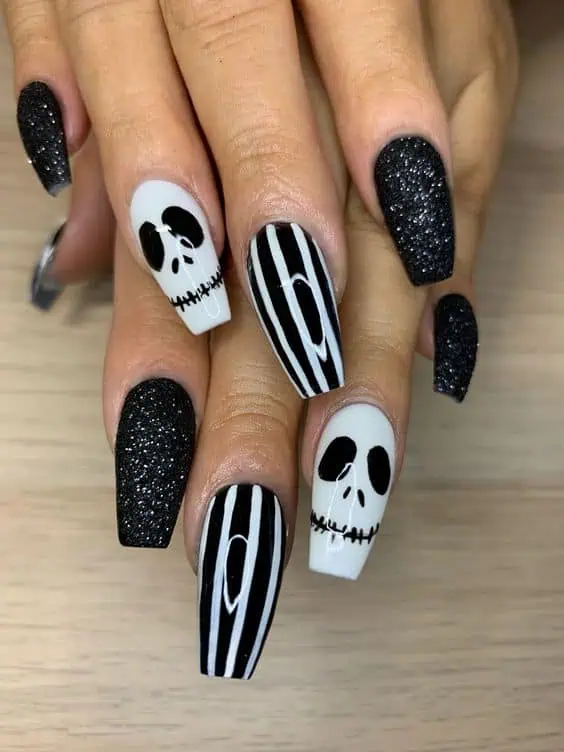 Disney Nightmare Before Christmas Halloween nails with a jack skellington design on the ring fingers, black and white stripes on the middle nails, and black glitter for the rest