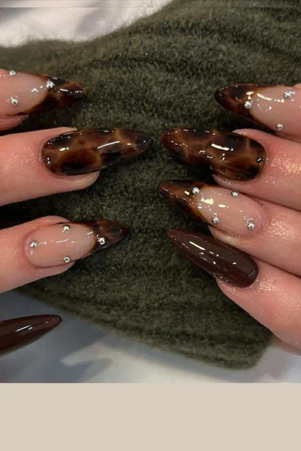 Glossy brown almond-shaped nails with a tortoiseshell leopard print design and silver rhinestone accents, perfect for an elegant autumn manicure.