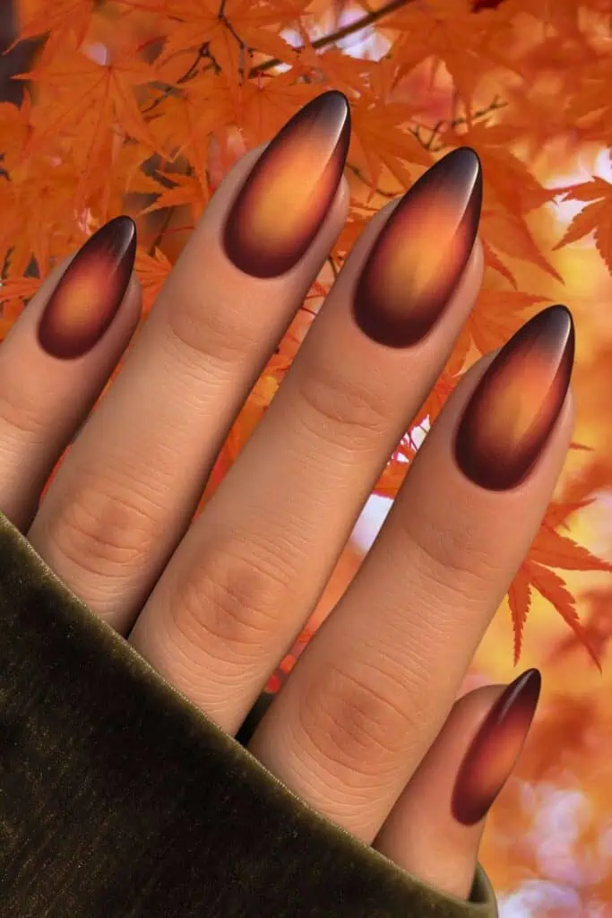 Almond-shaped nails with a gradient ombre design in burnt orange and deep brown tones, set against autumn leaves. Perfect for trending fall nail ideas in 2025.