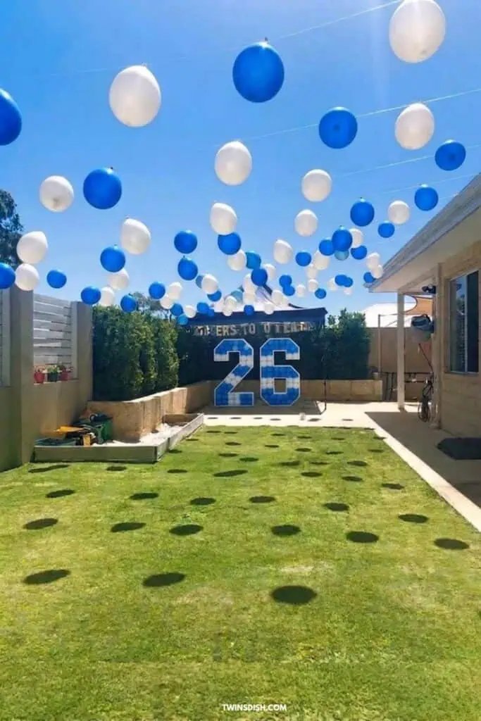 Blue and white balloon backyard graduation party setup with hanging balloons, lawn decor, and “Class of 2026” backdrop for a stylish outdoor grad celebration.