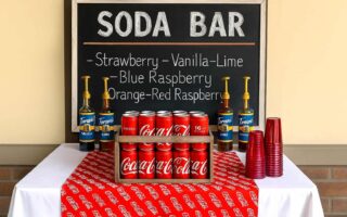 Outdoor boys’ graduation party soda bar with Coca-Cola crate, chalkboard sign, red cups, and classic drink syrups – fun and budget-friendly DIY party idea for High School, and College Grad guys.