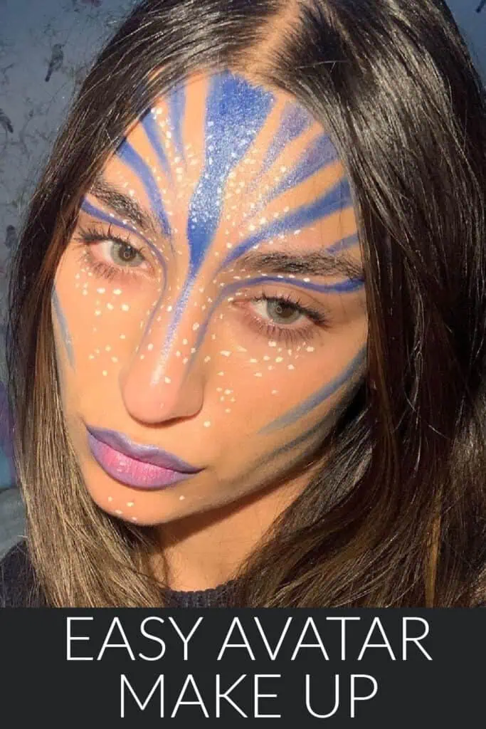 Close-up of easy Avatar-inspired makeup for Halloween. The woman’s face is painted with blue stripes, white dotted accents, and purple lips to resemble the Na’vi look from the Avatar movie. Simple DIY face paint idea for an Avatar Halloween costume.