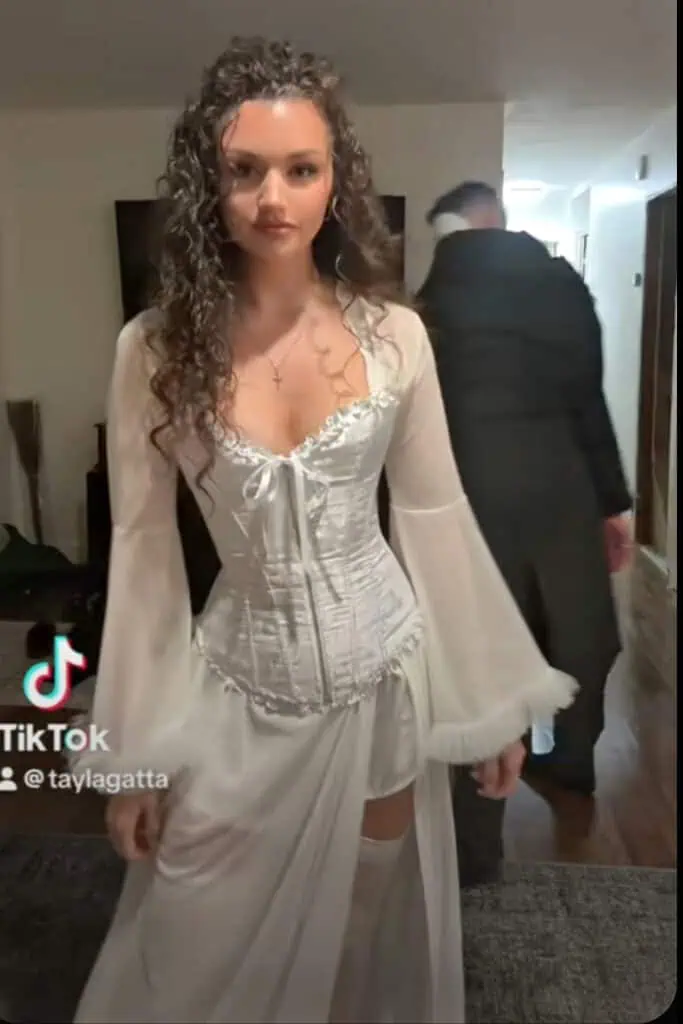 Woman dressed as Christine from The Phantom of the Opera wearing a flowing white corset gown with lace and sheer sleeves — elegant Halloween costume inspired by the classic musical.