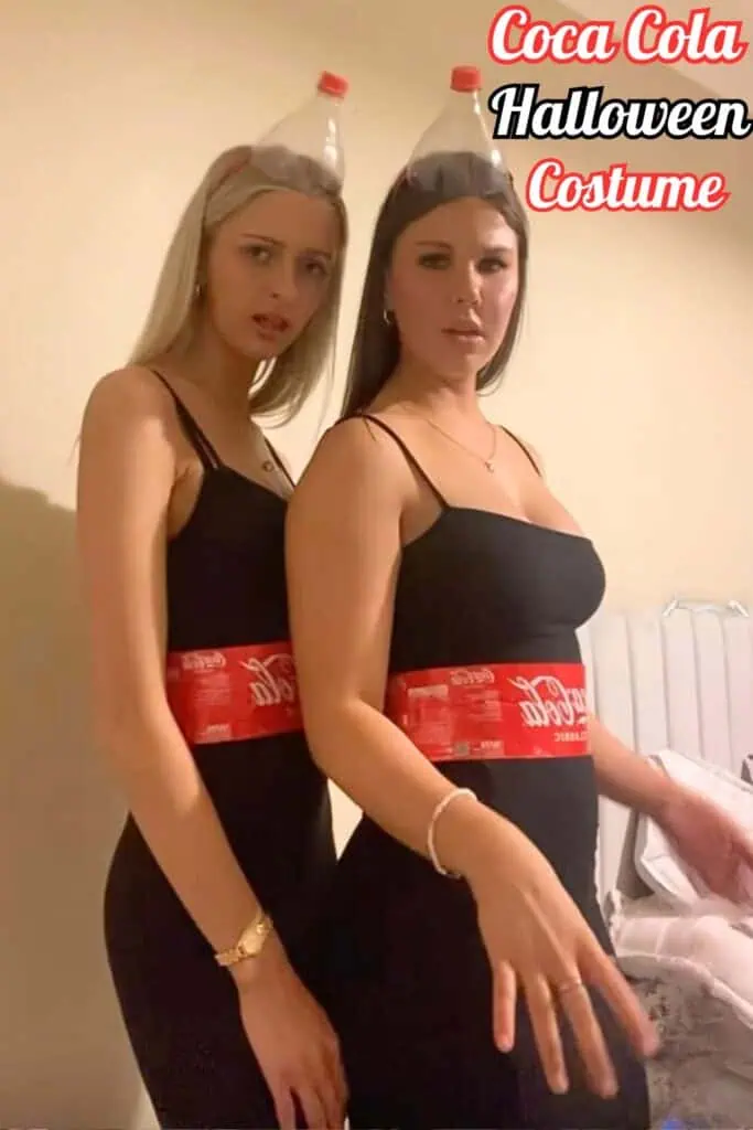 Two women dressed in DIY Coca-Cola Halloween costumes, wearing black dresses with Coca-Cola labels around their waists and plastic soda bottles as headpieces. A fun and creative Halloween costume idea for best friends or duos.