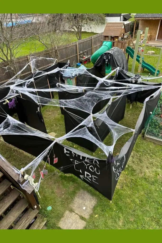 DIY outdoor Halloween haunted house maze made with black walls, spider webs, skeletons, and spooky decorations in a backyard