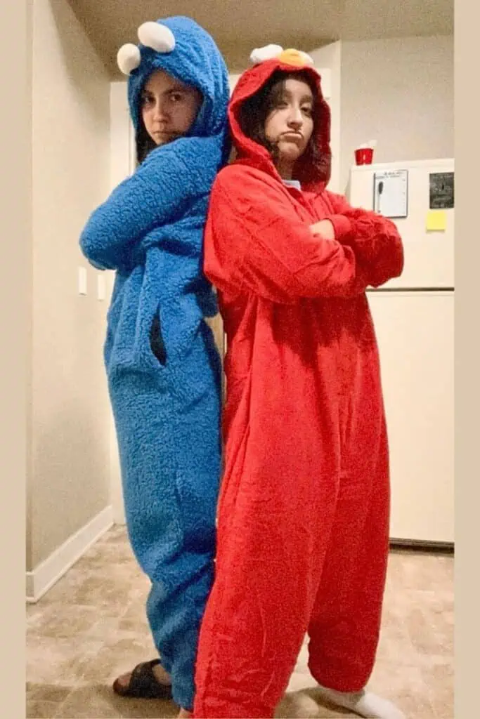 Two friends in Sesame Street-inspired Halloween costumes: one wearing a red Elmo onesie and the other in a blue Cookie Monster onesie. Cute and easy duo costume idea for BSF or BFF Halloween.