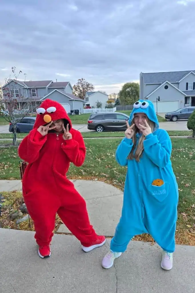 Two friends dressed in Sesame Street Halloween costumes, one wearing a red Elmo onesie and the other in a blue Cookie Monster onesie. Fun, cozy, and easy costume idea for Halloween, perfect for best friends or siblings.