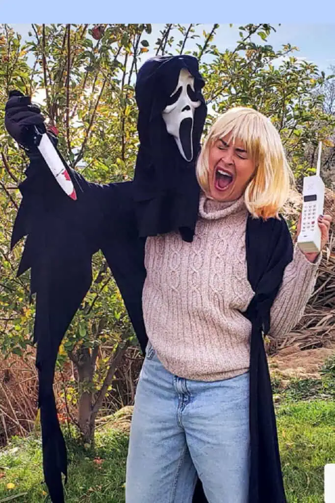 Funny Scream Halloween costume with Ghostface holding a knife and Drew Barrymore’s character in a blonde wig, sweater, jeans, and holding a vintage phone