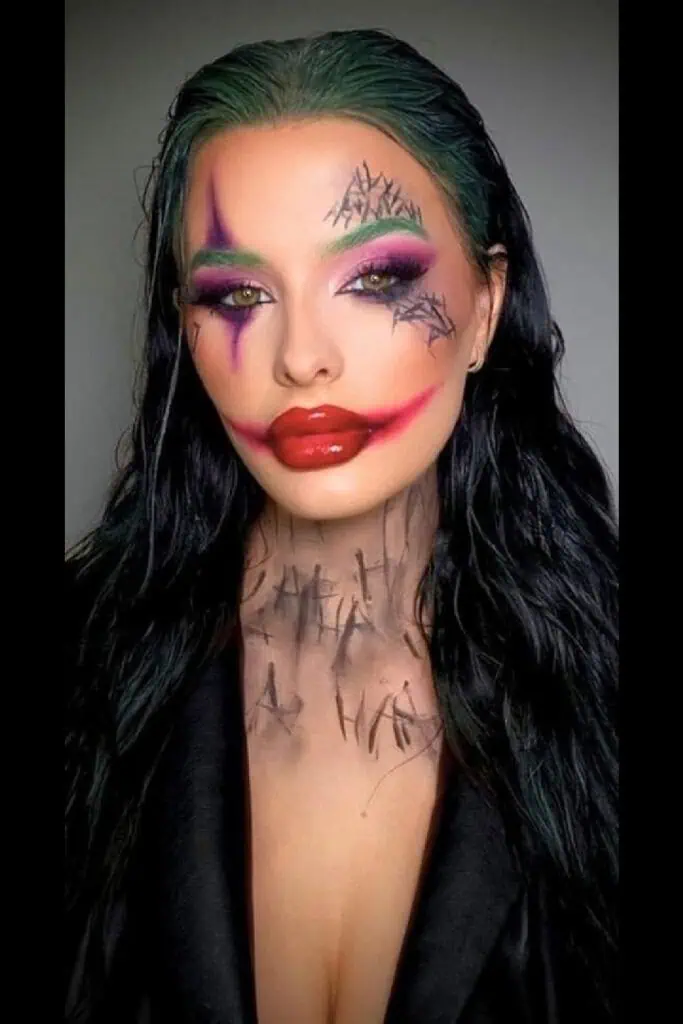 Woman in a Joker Halloween costume with green hair, smudged red lips, dramatic purple and black eye makeup, and “HA HA” writing on her neck. Creative and bold Halloween makeup idea for women.
