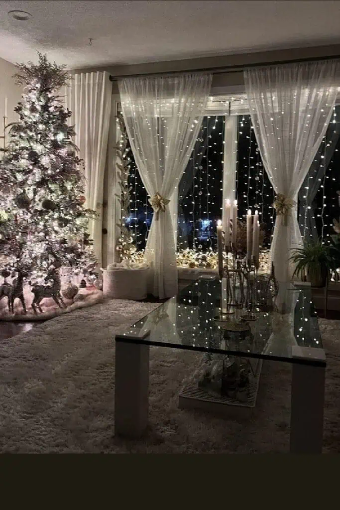 Cozy Christmas living room with sheer curtains and cascading fairy lights, a glowing tree, tall candles on a glass coffee table, and a plush neutral rug at night.