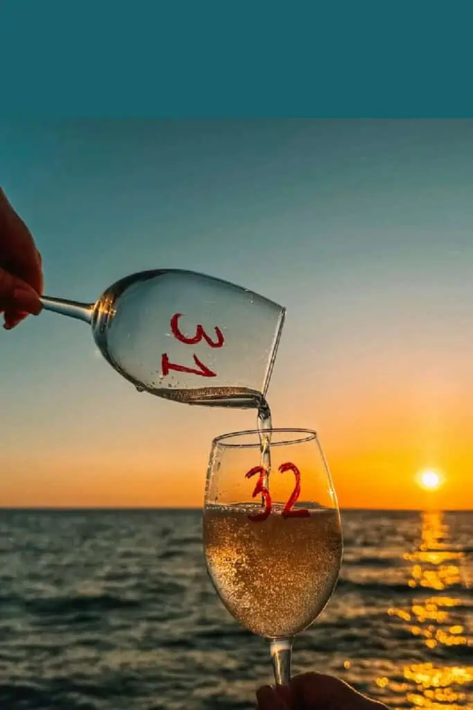 Creative birthday photo idea showing a “31” wine glass pouring into a “32” glass at sunset over the ocean—symbolizing one year flowing into the next. Perfect golden hour aesthetic for celebrating birthdays with meaning and style.