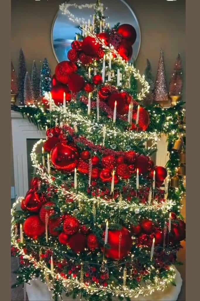 Elegant red spiral Christmas tree decorated with oversized red ornaments, glowing candles, cascading fairy lights, and garland—luxury holiday tree design idea for 2025.