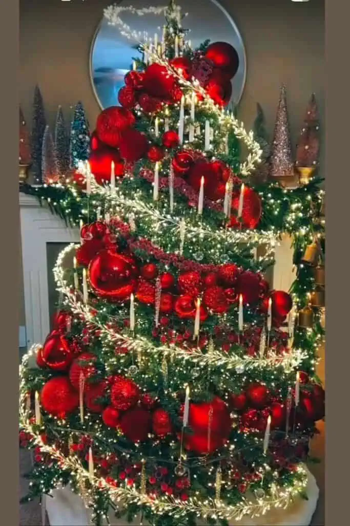 Elegant red spiral Christmas tree decorated with oversized red ornaments, glowing candles, cascading fairy lights, and garland—luxury holiday tree design idea for 2025.