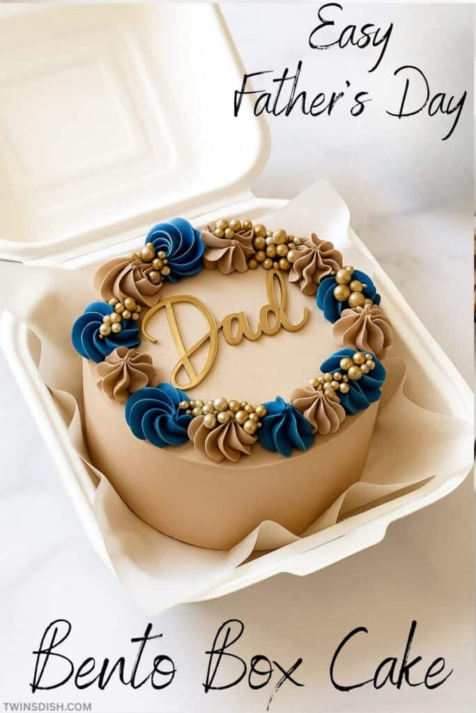 Father's Day Themed Bento Box Cake, small cake iced with chocolate and blue frosting, fancy piping and a gold "Dad" Cake decoration on top, cake is placed in a small take out box