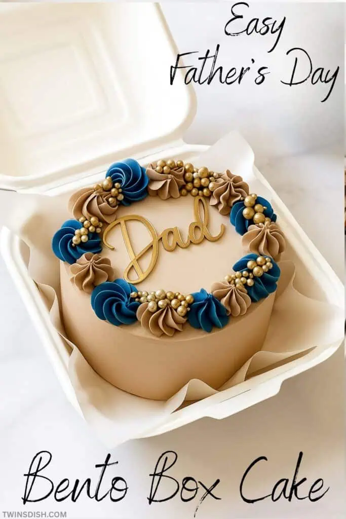 Father's Day Themed Bento Box Cake, small cake iced with chocolate and blue frosting, fancy piping and a gold "Dad" Cake decoration on top, cake is placed in a small take out box