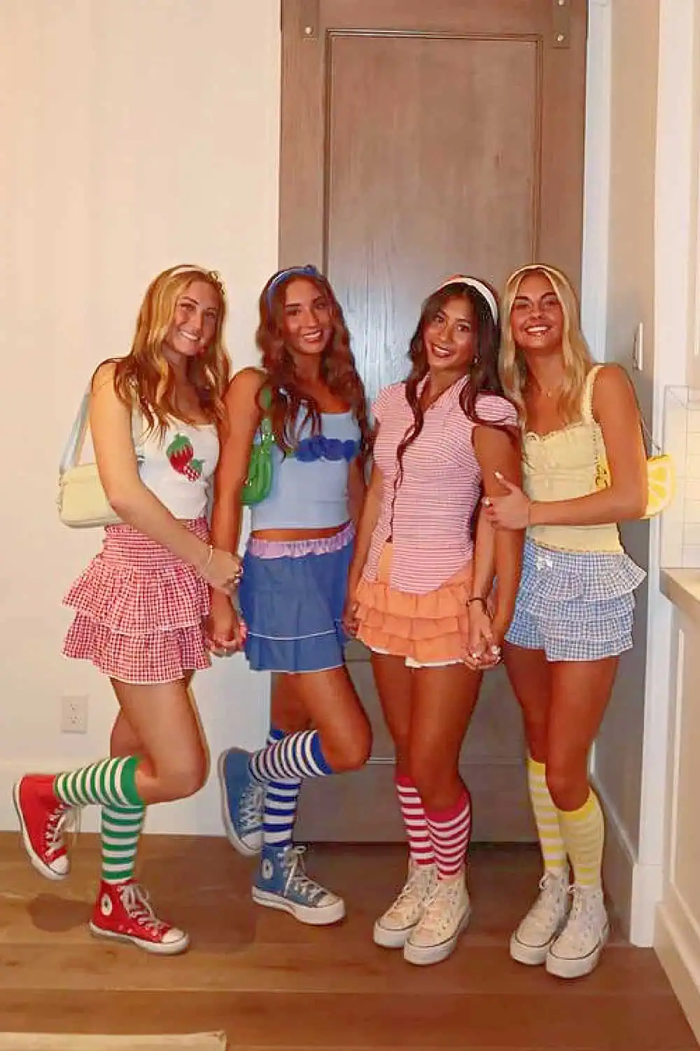 Group of four women in colorful Strawberry Shortcake–inspired Halloween costumes, each wearing mini skirts, striped socks, and coordinating accessories. Creative trio and group costume idea perfect for college, parties, or themed events.