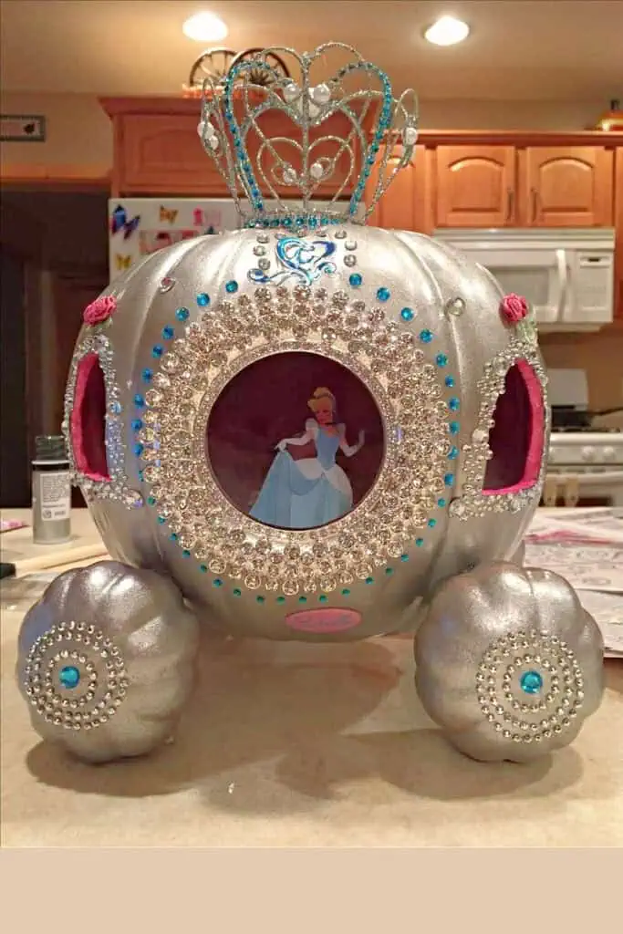 Silver Cinderella pumpkin carriage decoration made from a painted pumpkin with jeweled accents, crown topper, pink velvet windows, and an image of Cinderella in the center, perfect for a Disney princess-themed plastic pumpkin decorating craft or Halloween decor