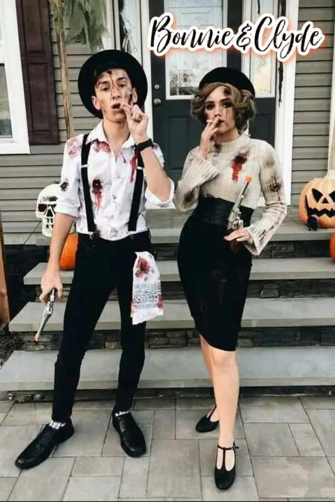 Couples Halloween costume idea as Bonnie and Clyde. A man wears suspenders, black pants, and a white shirt splattered with fake blood, holding a toy gun, while a woman wears a vintage-style skirt and blouse with a beret, also with blood details and holding a toy gun. Both pose together with cigarettes for a 1930s gangster outlaw look, standing outside decorated for Halloween.