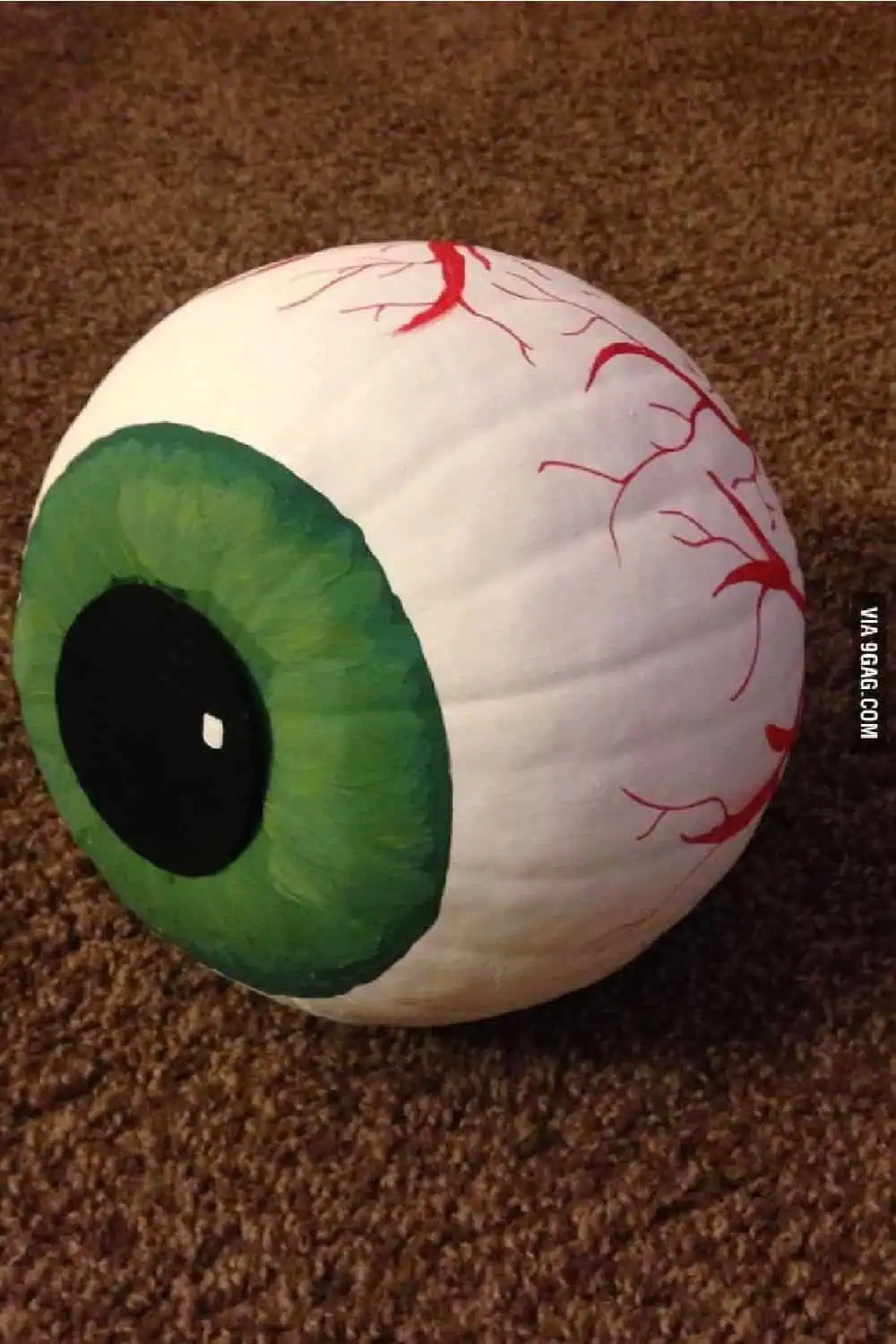 DIY eyeball pumpkin painting idea featuring a white painted pumpkin with green iris and red veins, designed to look like a spooky eyeball for Halloween decor.