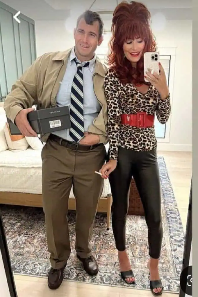 Couple dressed as Peggy and Al Bundy for Halloween. The woman wears a teased red wig, leopard print top, red belt, and black leather pants, while the man wears a rumpled shirt and tie, tan pants, and holds a shoebox, recreating the classic Married With Children look.